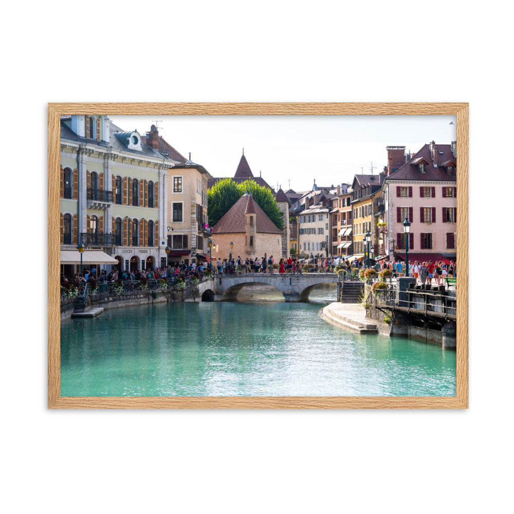 Vue estivale d'Annecy, mettant en lumière le Pont Perrière et le Palais de l'Île, encadrée d'un bois de chêne.