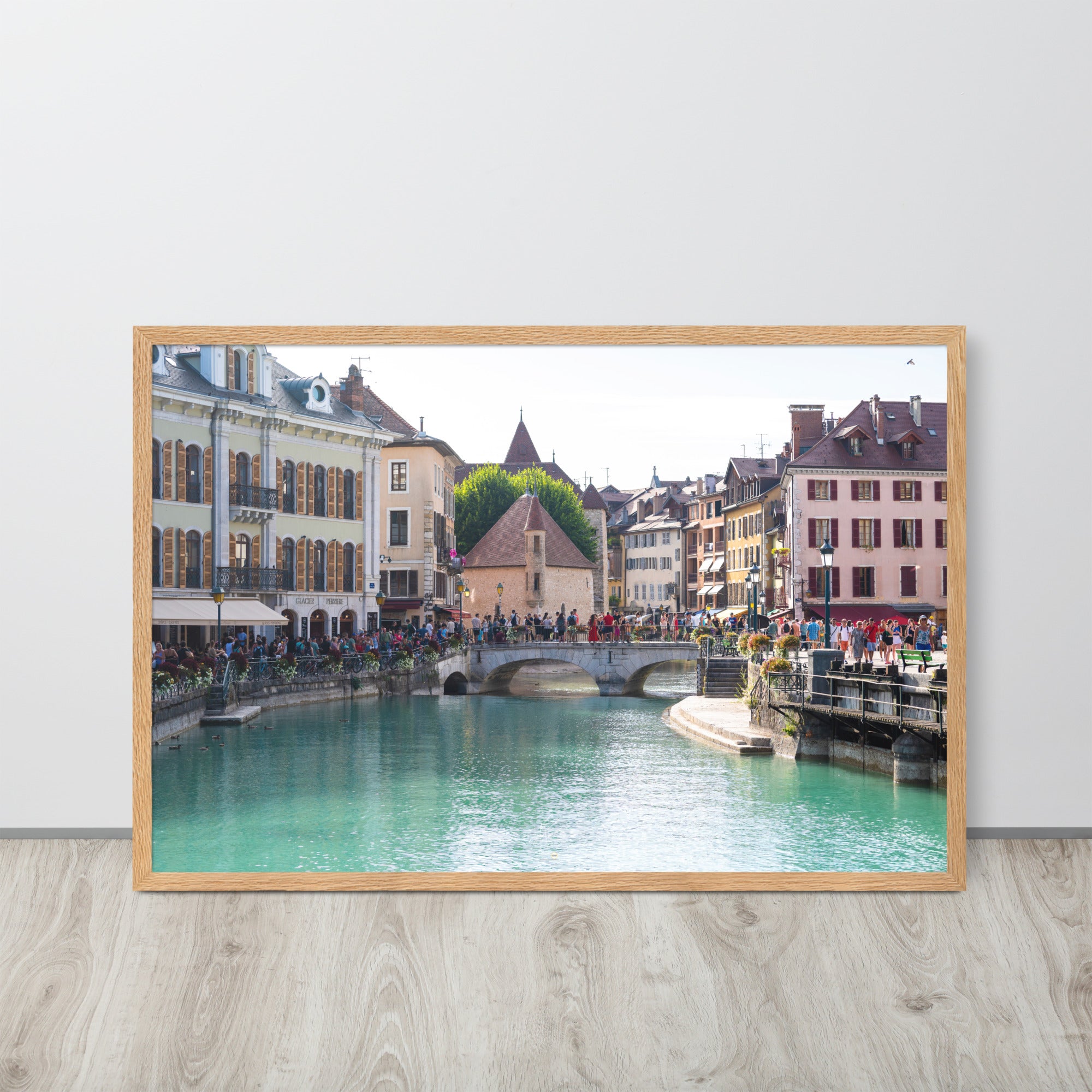 Vue estivale d'Annecy, mettant en lumière le Pont Perrière et le Palais de l'Île, encadrée d'un bois de chêne.
