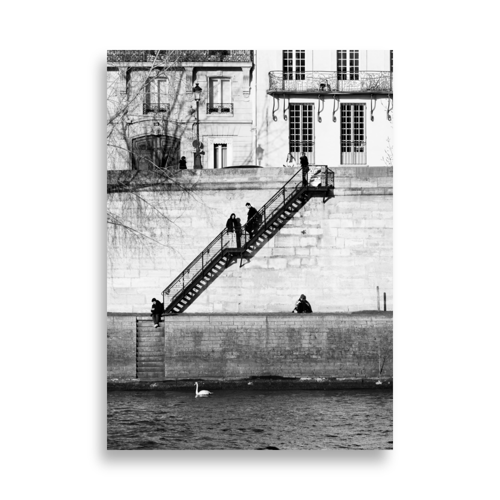 Photographie noir et blanc de personnes installées tranquillement sur les quais à Paris, encadrées par deux escaliers symétriques.