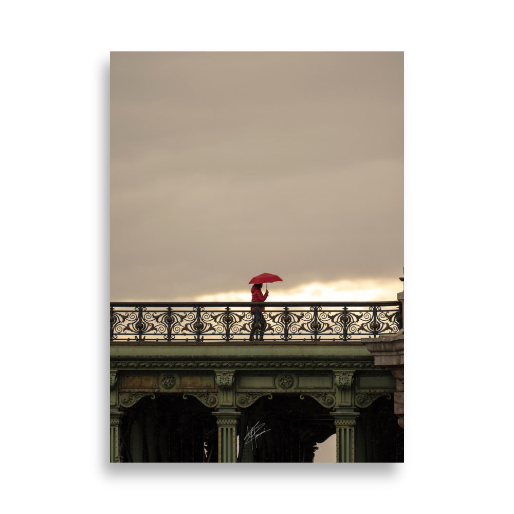 Photographie d'une femme traversant un pont parisien avec un parapluie rouge vif sur fond de paysage pluvieux.