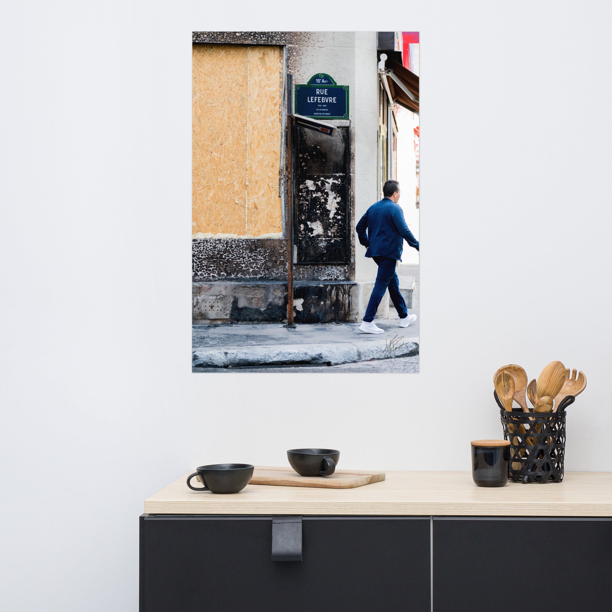 Photographie de la "Rue Lefebvre" après un incendie, montrant des traces de suie, un panneau de sens interdit plié et un passant.