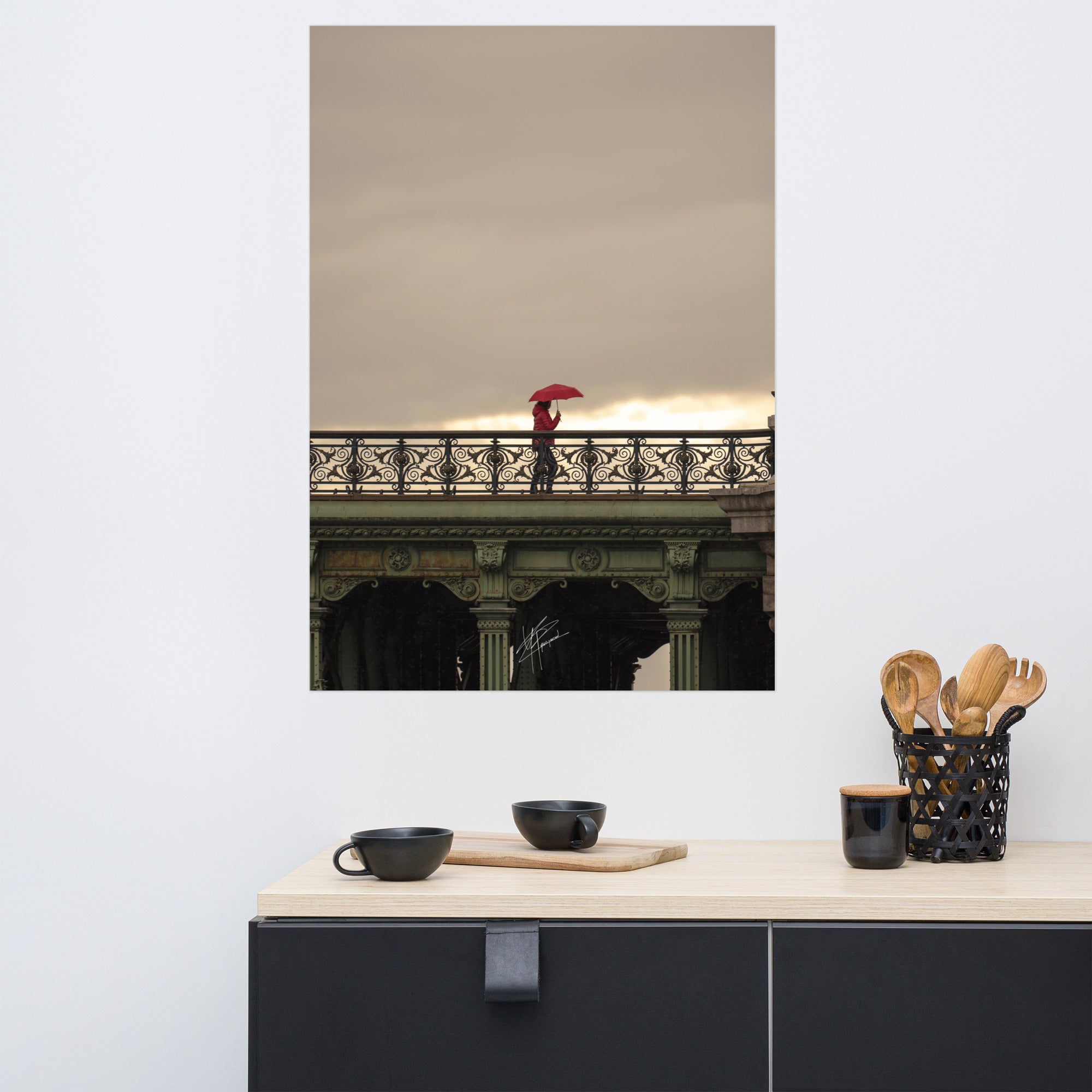 Photographie d'une femme traversant un pont parisien avec un parapluie rouge vif sur fond de paysage pluvieux.